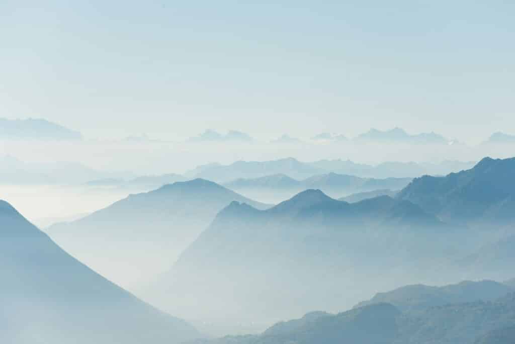 Foggy mountain landscape with layers of peaks under a clear blue sky.