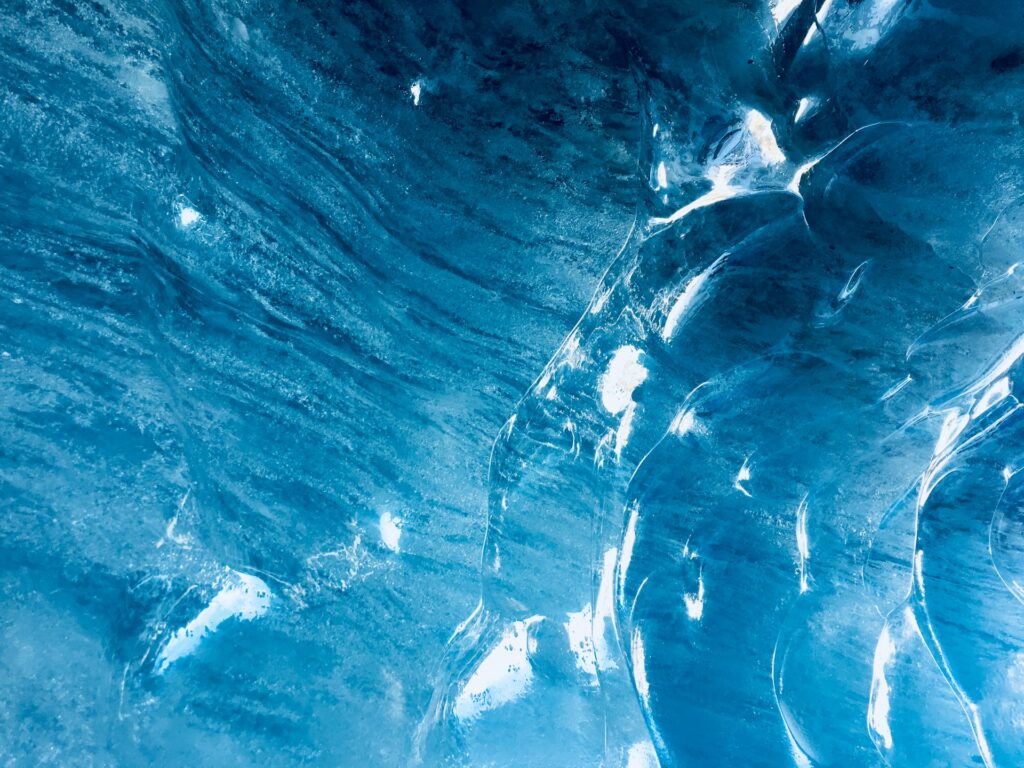 Close-up of blue ice texture in a glacial cave, showing intricate patterns and light reflections.