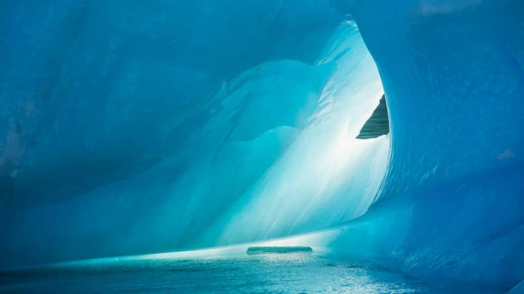 Interior of a vibrant blue ice cave with a small pool of water reflecting light.