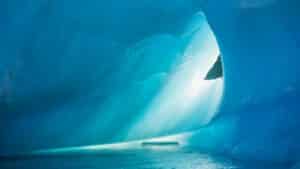 Interior of a vibrant blue ice cave with a small pool of water reflecting light.