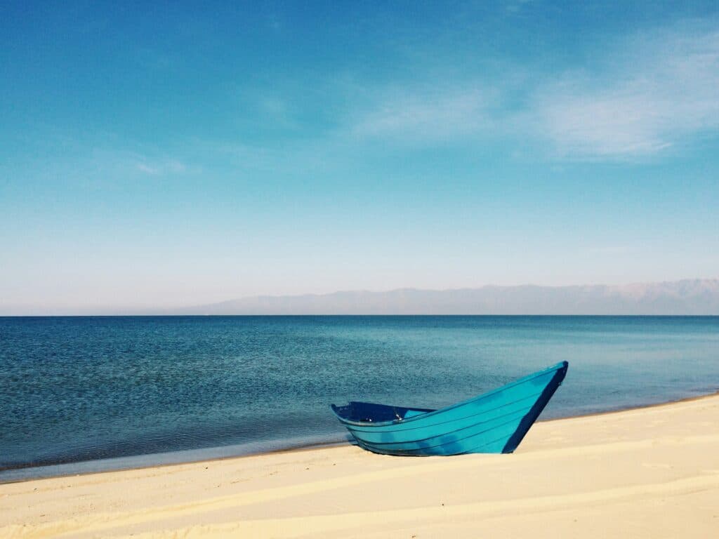 Blue boat on a sandy beach with clear skies and mountains in the background.