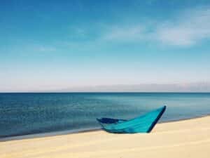 Blue boat on a sandy beach with clear skies and mountains in the background.