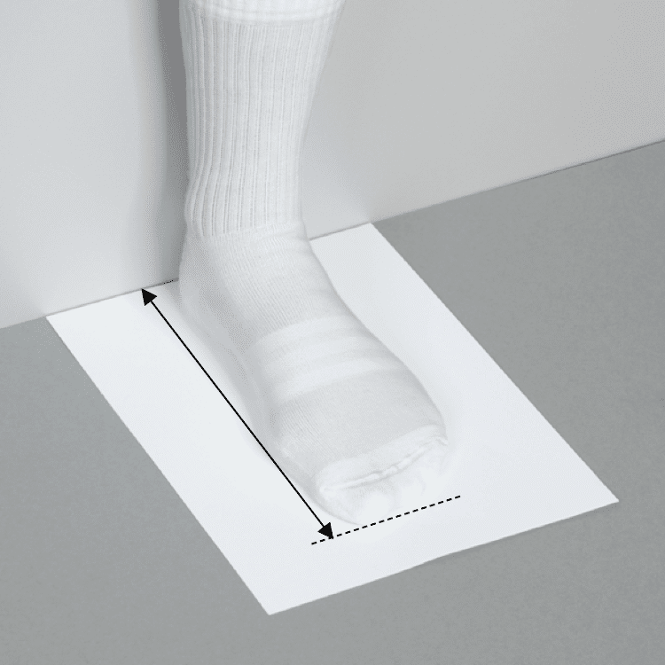 Foot in white sock on paper with measurement lines for size.