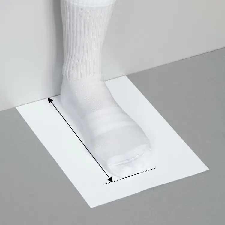 Foot in white sock on paper with measurement lines for size.