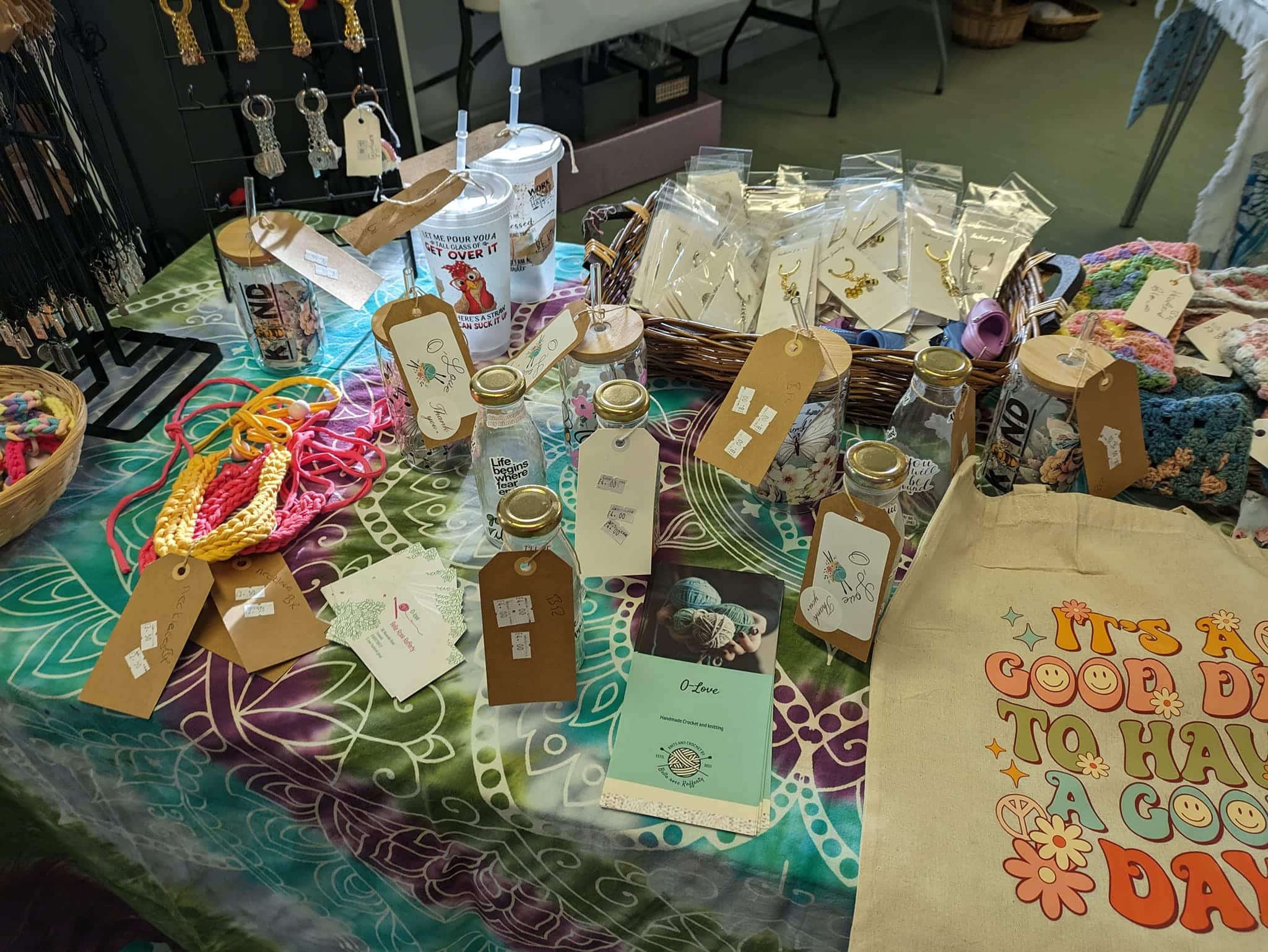 Craft fair table with handmade items, including keychains, embroidered bags, crochet accessories, and decorated jars.