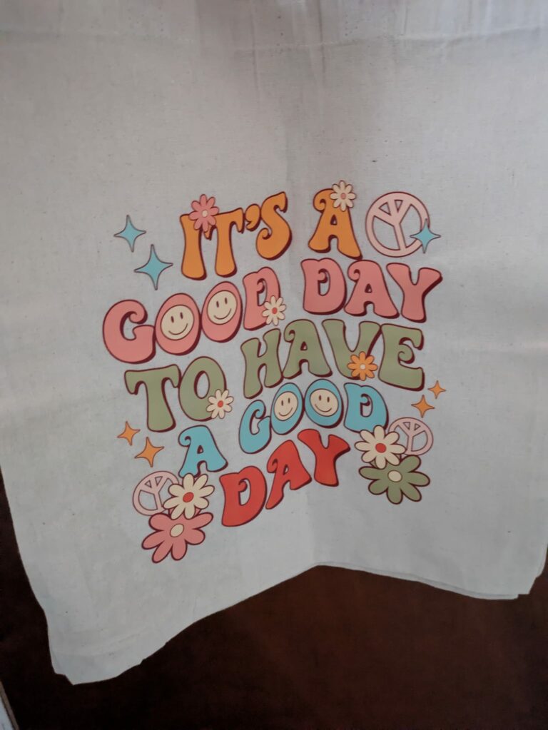 Colorful text on fabric reading "It's a good day to have a good day" with smiley faces and peace symbols.
