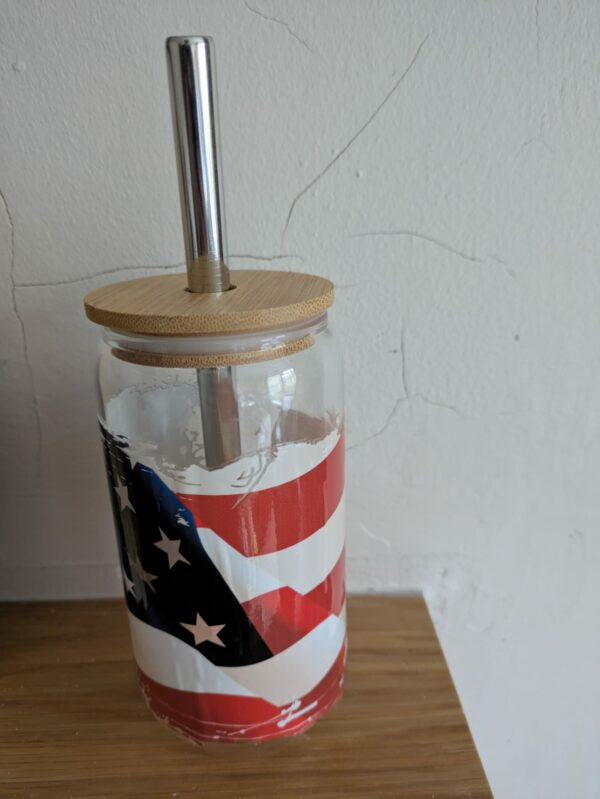 Glass tumbler with American flag design, bamboo lid, and metal straw on a wooden surface.