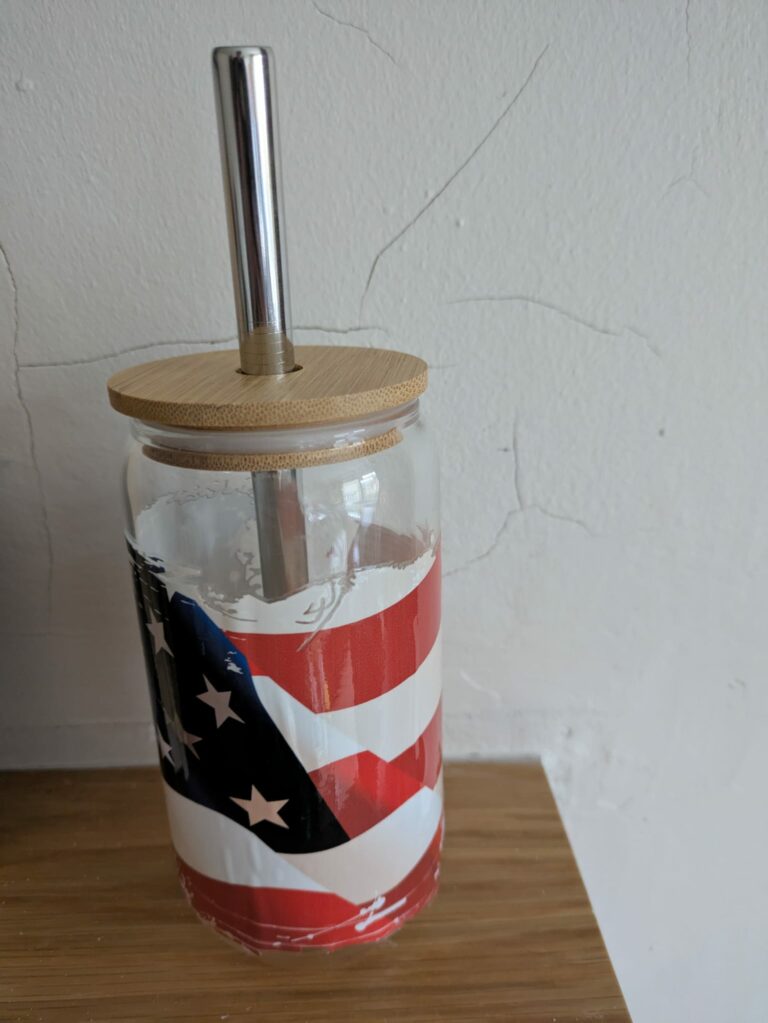 Glass tumbler with American flag design, bamboo lid, and metal straw on a wooden surface.