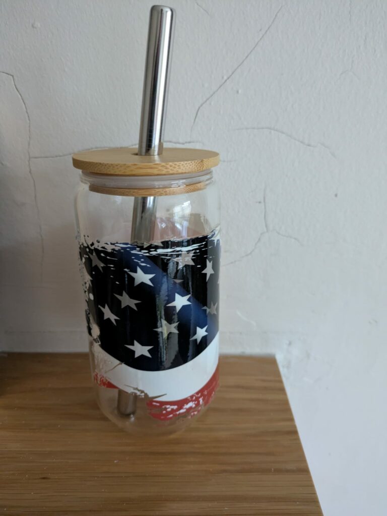 Glass jar with American flag design, bamboo lid, and metal straw on wooden surface.