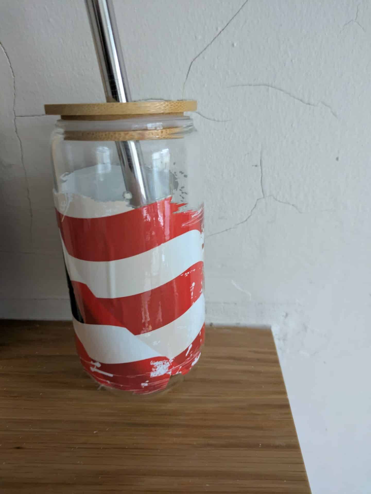 Glass jar with red and white stripes, bamboo lid, and metal straw on a wooden surface.