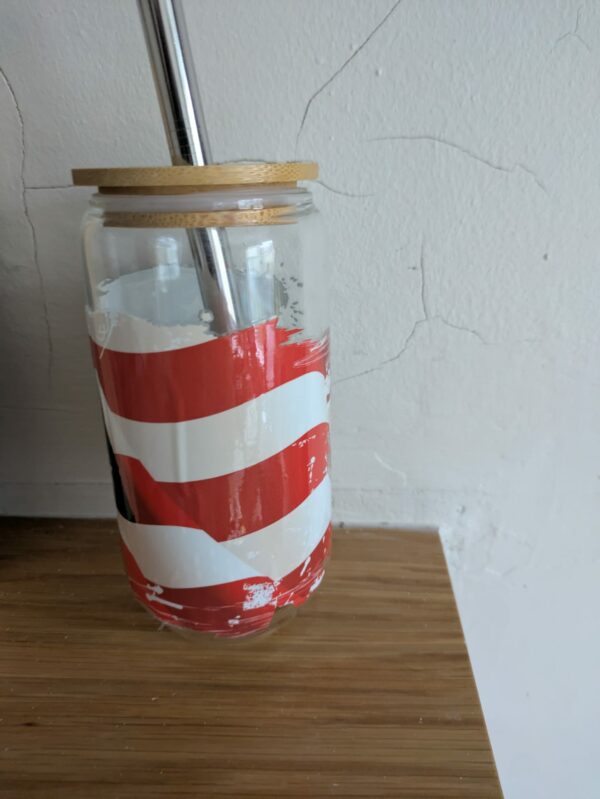 Glass jar with red and white stripes, bamboo lid, and metal straw on a wooden surface.