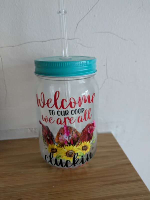 Decorative mason jar with a teal lid, straw, and chicken-themed design.