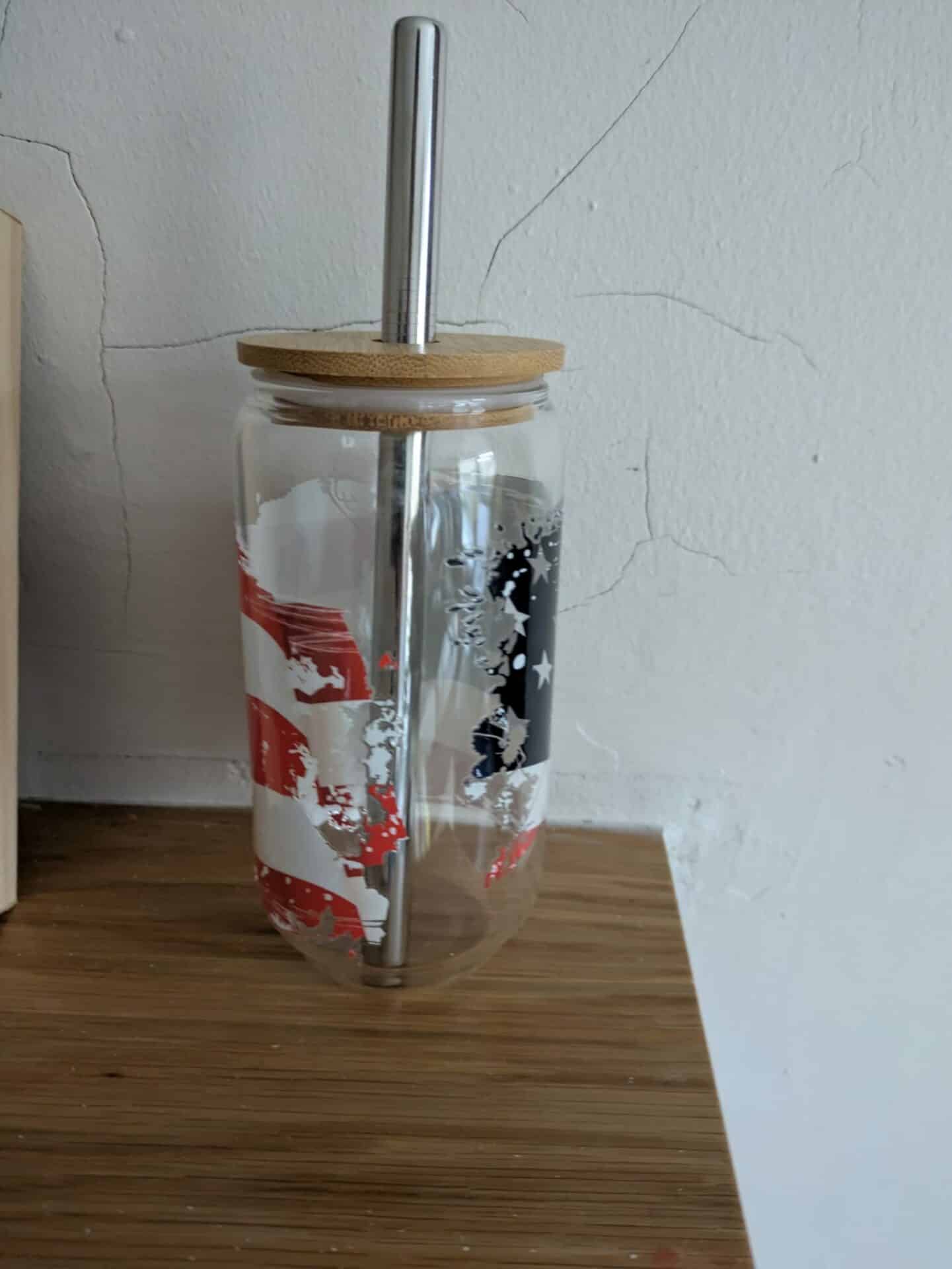 Glass jar with American flag design, topped with a wooden lid and metal straw, placed on a wooden surface.