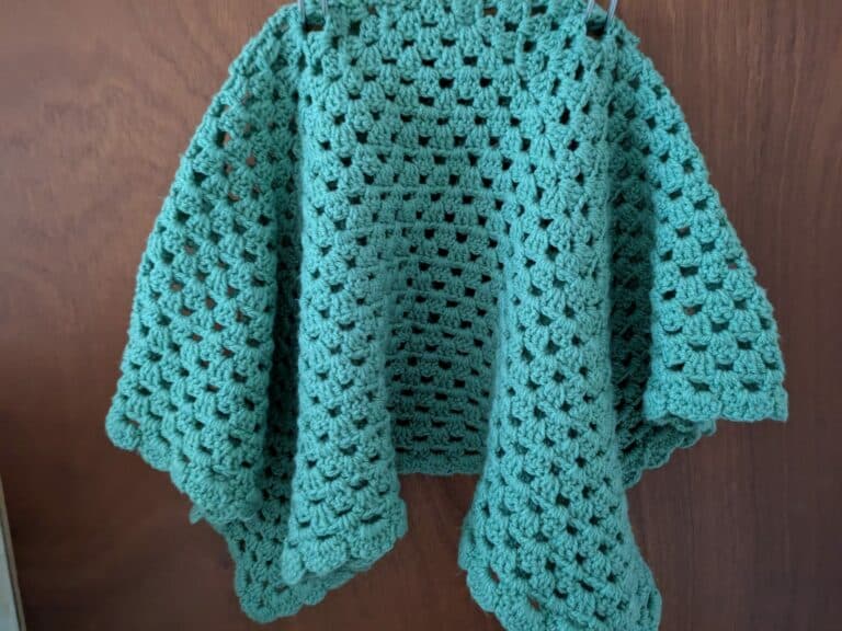 Green crocheted shawl hanging against a wooden background.