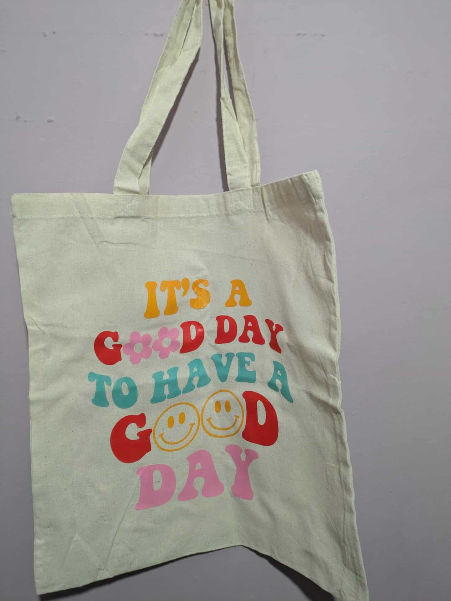 Canvas tote bag with colorful text and smiley faces reading "It's a good day to have a good day."