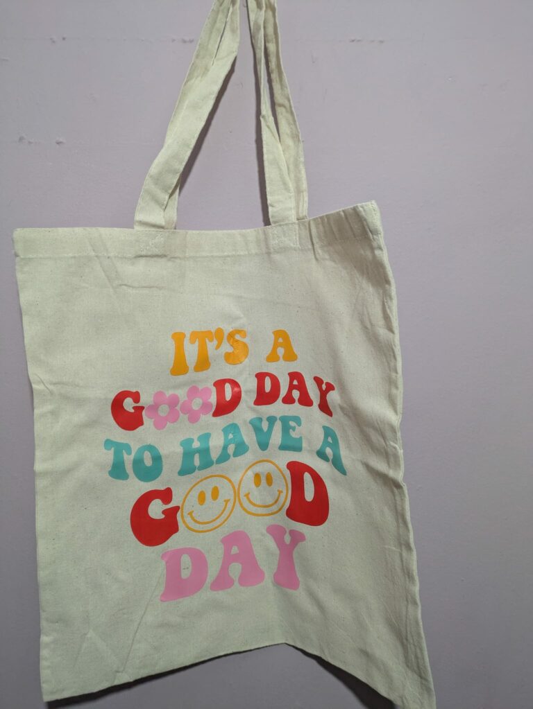 Canvas tote bag with colorful text and smiley faces reading "It's a good day to have a good day."