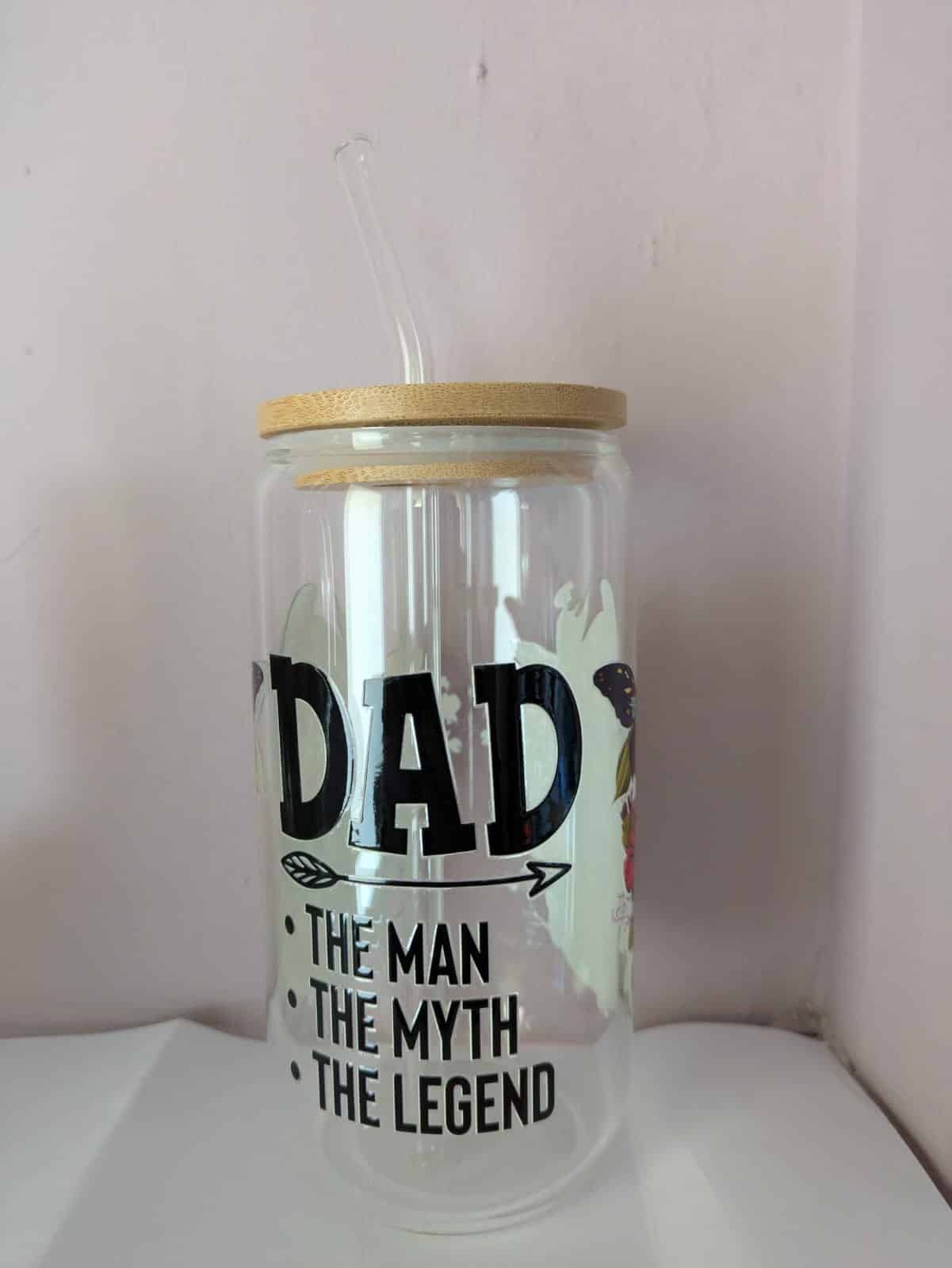 Glass tumbler with straw, wood lid, and text: "Dad, The Man, The Myth, The Legend" on a light background.