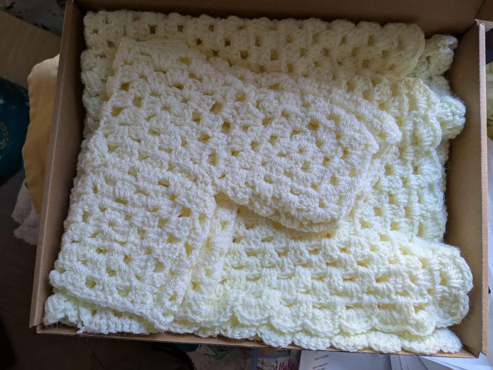 Yellow crocheted blanket and mittens in a cardboard box.