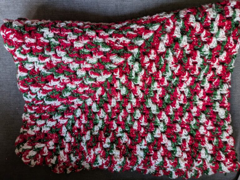 Crocheted pillow with red, green, and white yarn pattern on a gray background.