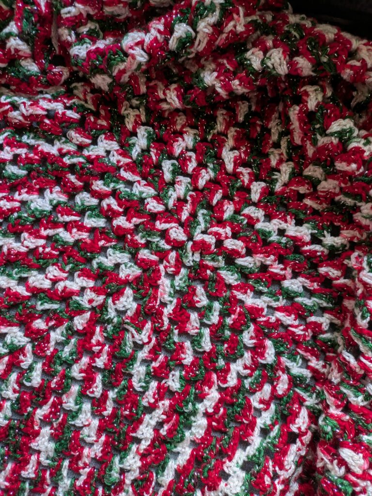 Close-up of a knitted pattern with red, green, and white yarn with a spiral design.