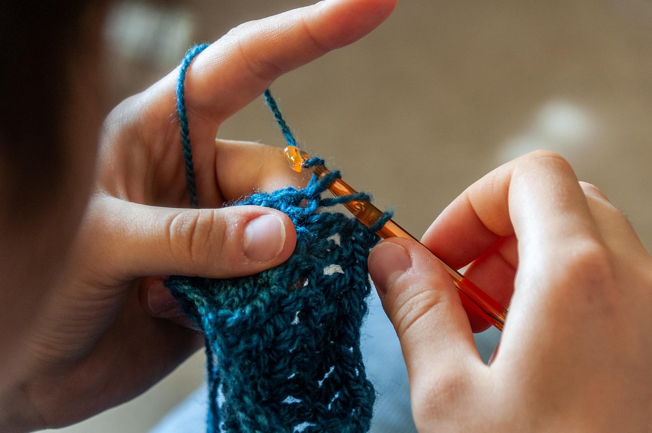 Hands crocheting blue yarn with an orange hook.